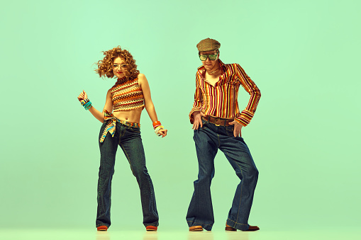 Incendiary dance. Emotional man and woman in retro style clothes dancing disco dance over green background. Concept of fashion trends of 70s, 1980s years, music, hippie lifestyle