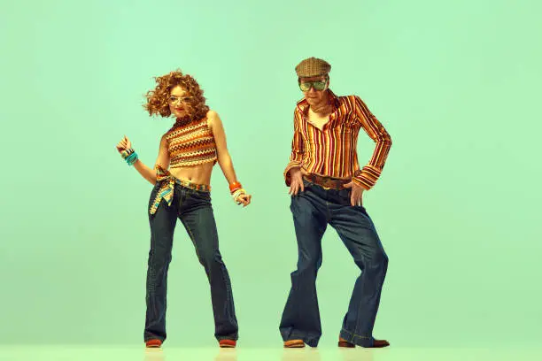 Photo of Incendiary dance. Emotional man and woman in retro style clothes dancing disco dance over green background. Concept of fashion trends of 70s, 1980s years, music