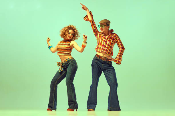 Two excited people, man and woman in retro style clothes dancing disco dance over green background. 1970s, 1980s fashion, music, hippie lifestyle, Happy and active dancers. Two excited people, man and woman in retro style clothes dancing disco dance over green background. 1970s, 1980s fashion, music, hippie lifestyle 1970s woman stock pictures, royalty-free photos & images