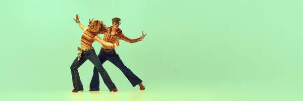 Photo of Incendiary dance. Emotional man and woman in retro style clothes dancing disco dance over green background. Concept of fashion trends of 70s, 1980s years, music