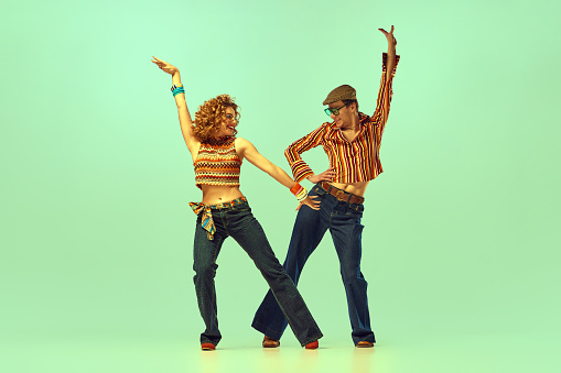 Incendiary dance. Emotional man and woman in retro style clothes dancing disco dance over green background. Concept of fashion trends of 70s, 1980s years, music, hippie lifestyle