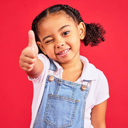 Thumbs up, portrait and girl child in studio, red background or isolated hand sign. Happy kids, thumb gesture and wink face of like emoji, support and vote of trust, thanks or yes agreement of review