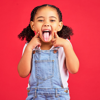 Little girl, portrait and tongue out on isolated red background in goofy, silly games and playful facial expression. Happy, kid and child with funny face in comic emoji, charades and studio activity