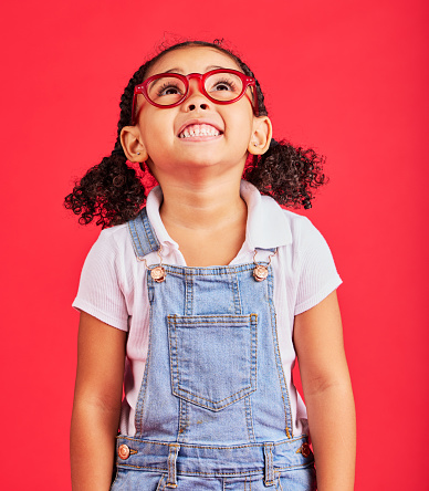 Looking up, child and fashion glasses on red background in kids style, eyes care and wellness health insurance. Smile, happy and little girl with optometry frames, vision support or retail sales deal