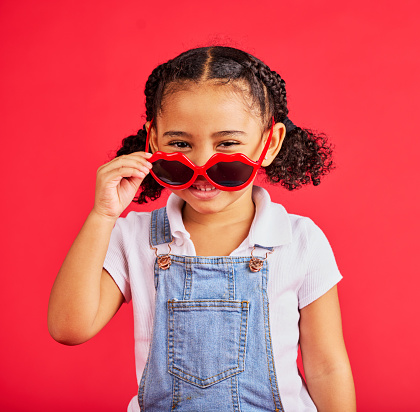 Child portrait, fashion and glasses on isolated red background in summer trend, holiday style and cool vacation. Smile, happy and kid with sunglasses for eyes healthcare, wellness and sun protection