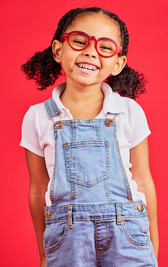 Happy child, portrait or fashion glasses on red background in children style, eyes care or wellness health. Smile, kid or little girl and optometry frames for cool vision support or medical insurance