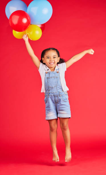 little girl, portrait or jumping with balloons on isolated red background for birthday party, celebration or fun event. smile, happy or energy child with air, flying or inflatable accessory in studio - celebration inflatable excitement concepts imagens e fotografias de stock