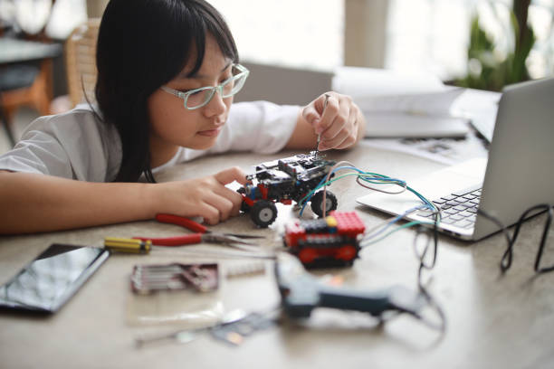 A young Asian girl is working on a robotic car for a science project as part of remote learning for her school's science and technology program, using her laptop at home. A young Asian girl is working on a robotic car for a science project. She is participating in her school's science and technology program through remote learning and using her laptop at home girl flex stock pictures, royalty-free photos & images