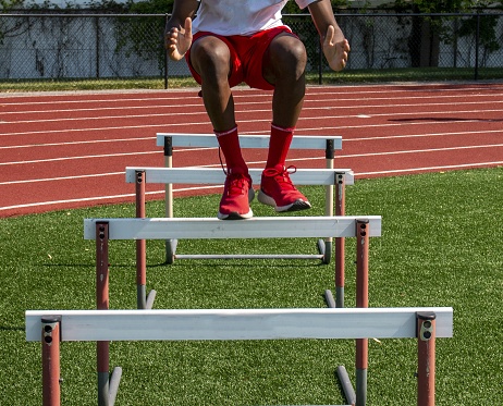 High school boy jumping over track hurdles for strength and flexibility