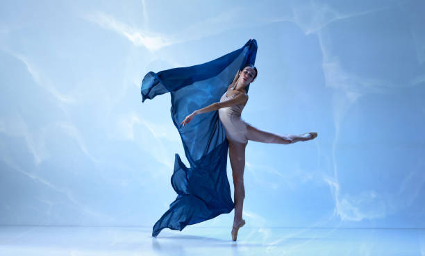 istock Ballerina dancing graceful movement with silk fabric over blue background 1477521737