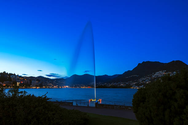 night view of a fountain in the middle of the lake with city lights behind - ticino canton mountain lake lugano lake imagens e fotografias de stock