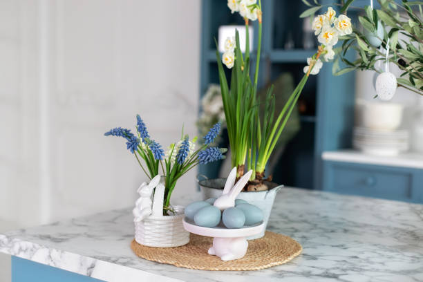 istock Flowers in vase, festive utensil and plate with easter blue eggs on table in kitchen. Home interior with easter decor. Spring Daffodils flowers in pot. Easter bunny. 1477526110