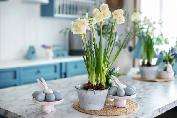 istock Flowers in vase, festive utensil and plate with easter blue eggs on table in kitchen. Home interior with easter decor. Spring Daffodils flowers in pot. Easter bunny. 1477526129