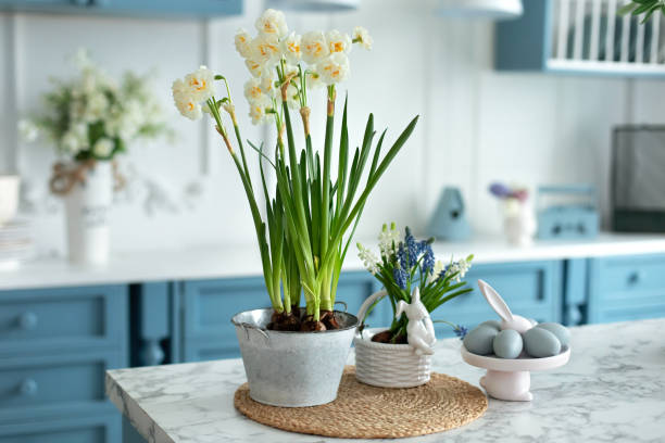 istock Flowers in vase, festive utensil and plate with easter blue eggs on table in kitchen. Home interior with easter decor. Spring Daffodils flowers in pot. Easter bunny. 1477526167