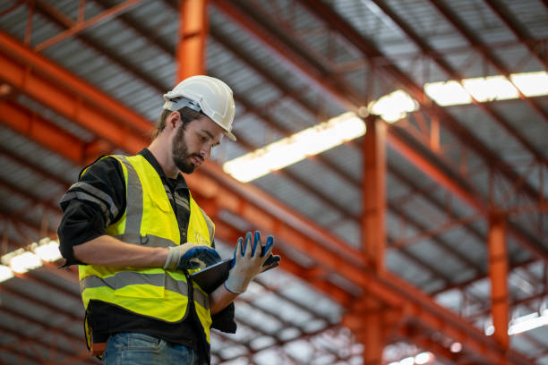istock Low angle view of a worker wearing reflective jacket holding digital tablet standing in factory warehouse 1477526736