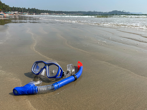 Stock photo of showing close-up view of sandy beach at low tide with scuba mask and snorkel left at water's edge.