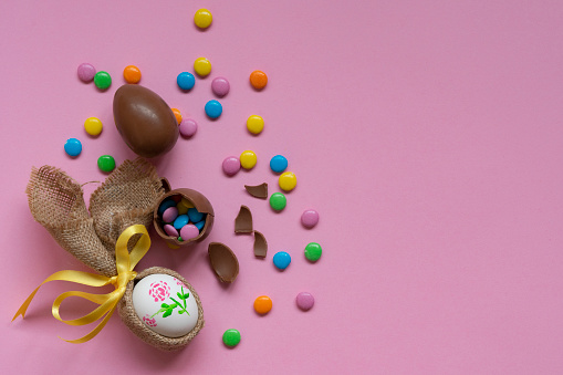 Close-up of Easter basket filled with Easter grass, candy eggs, mini carrots, and a chocolate rabbit on white background