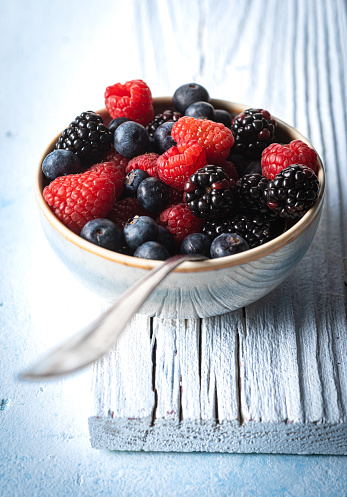 Bowl with raspberries, blackberries and blueberries on white background