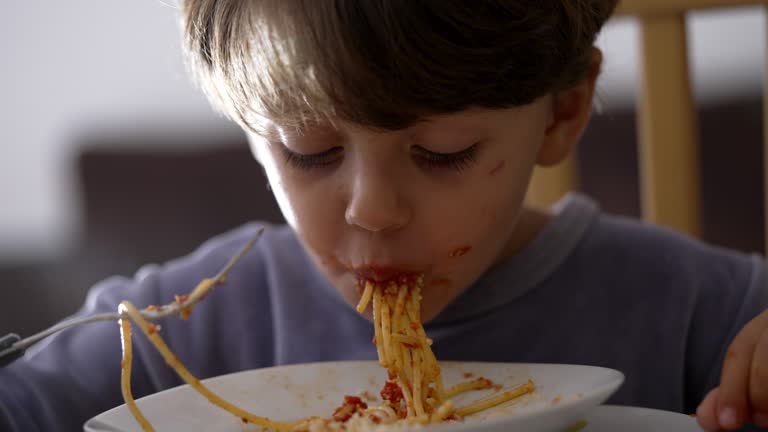 Close up child hands twisting spaghetti on plate. One small boy eats pasta. Italian food