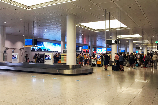 Passengers waiting at the baggage reclaim area in Munich Airport  looking for signs to direct them to the correct conveyor belt for their flight, keep an eye on the baggage and be ready to collect it as soon as it appears, before proceeding to customs and choosing from the various transportation options available to continue their journey.