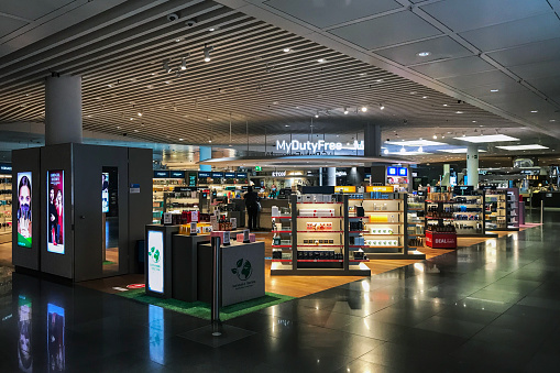 Duty-free store is a retail store located in Munich airports, that offers tax and duty-free goods to international travelers who are leaving or entering the country and typically include products such as alcohol, tobacco, perfume, cosmetics, electronics, and luxury items such as jewelry and watches. A few person shopping inside.