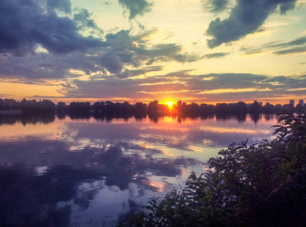 istock Sunset on the lake. Smooth water surface, clouds and sun. Calm summer evening. 1477537436