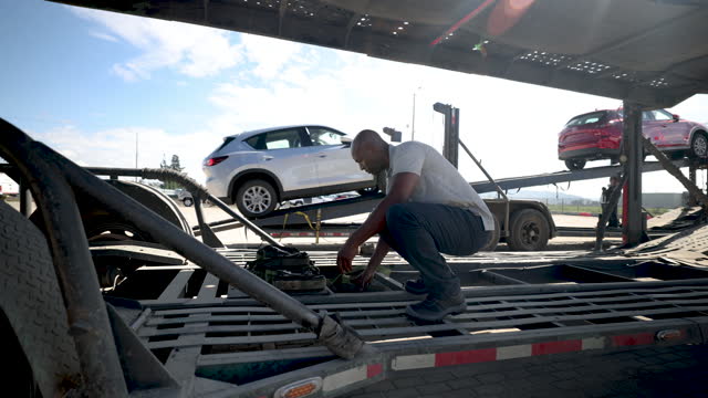 Black male car transporter rolling straps on the carrier after unloading a shipment