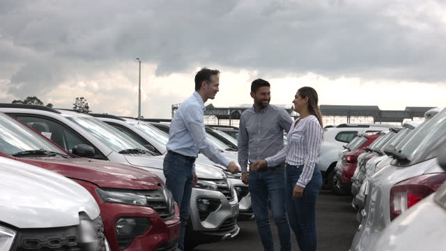 Salesman handshaking after closing a deal with a happy heterosexual couple at the car dealership