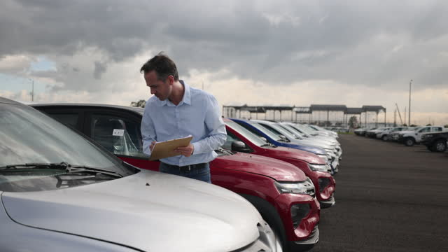 Male employee at a car distribution center doing an inventory of a new car