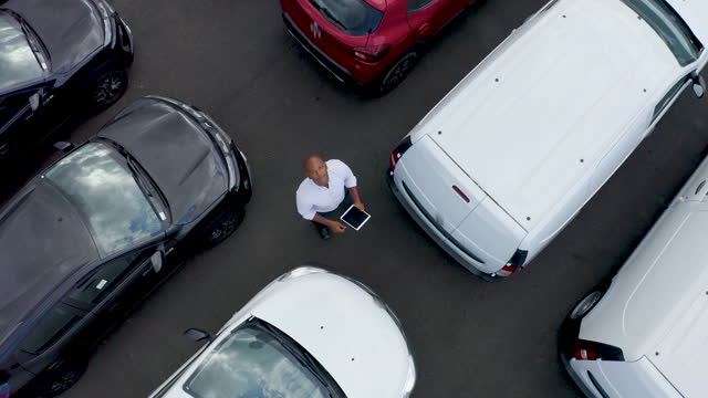 African American salesman using a tablet and facing up to the camera at an outdoor dealership