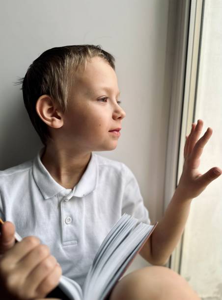 istock a boy in a white shirt looks out the window 1477540130