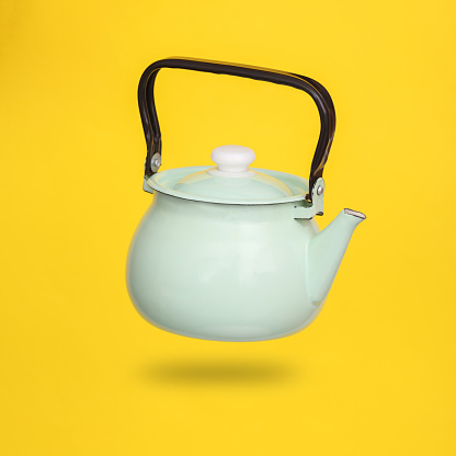 Metal ceramic teapot levitating on yellow background with shadow