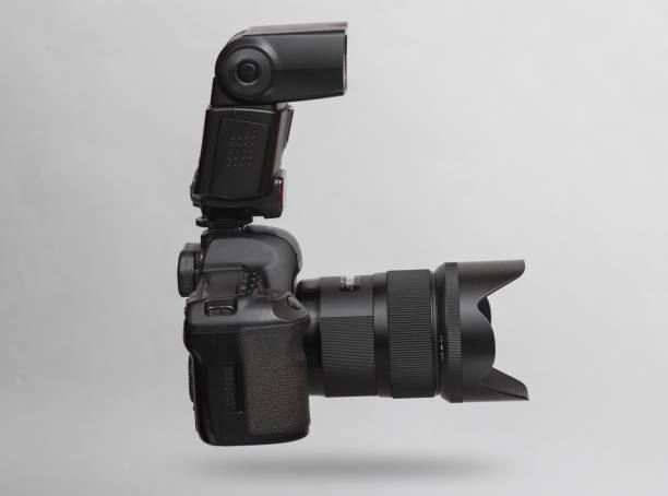 istock Modern digital dslr camera with lens and flash levitating on gray background with shadow 1477543446