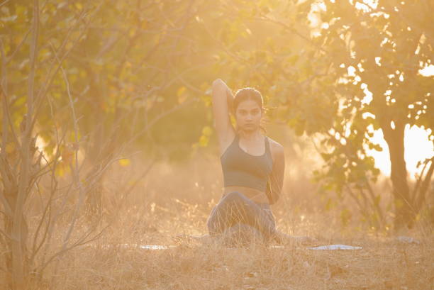 Yoga Asana poses by young woman in beautiful nature outdoors sitting crosslegged holding hands behind back stock photo