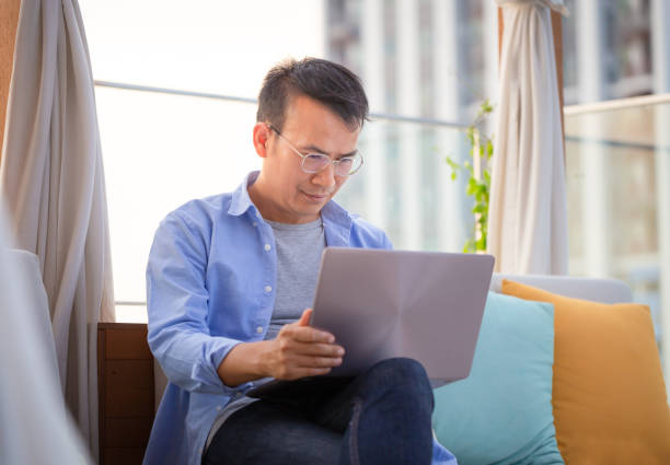 istock Asian man using laptop sitting on sofa at home, Man working from a laptop at the terrace 1477548488