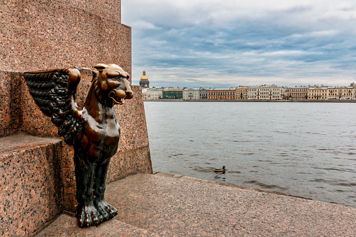Sculpture of Griffin - bronze winged lions 1834 on the University Embankment of the Neva river with the background view of Isaac Cathedral, Saint-Petersburg, Russia