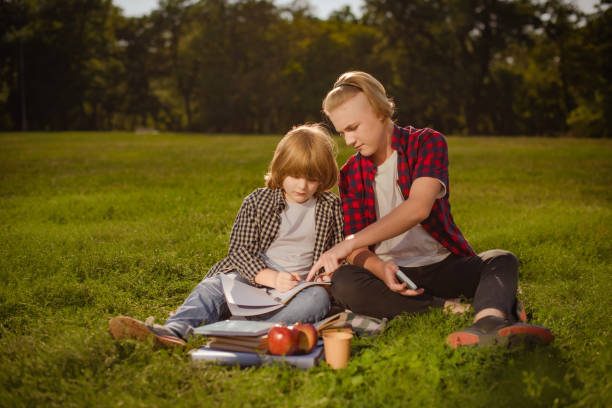 istock two boys doing homework on green grass where the older school boy is teaching the younger boy 1477550726