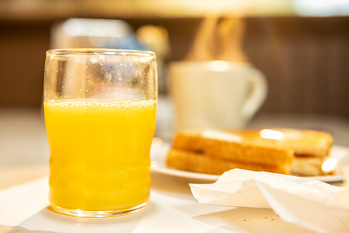 A sunrise breakfast of orange juice, toasted bread and a steaming hot cup of coffee in a diner.