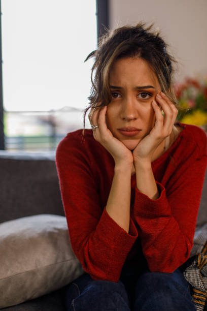 istock Sad young woman sitting with head in hands, worrying, looking at camera 1477557029