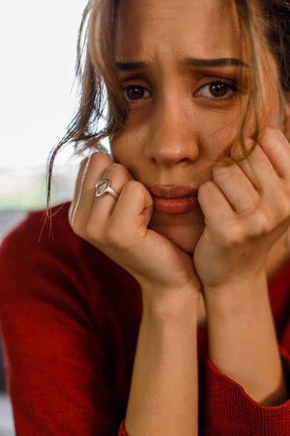 istock Sad young woman sitting with head in hands, worrying, looking at camera 1477557043