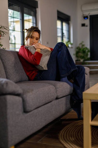 istock Young woman sitting on the sofa, embracing a pillow while feeling anxious 1477558391