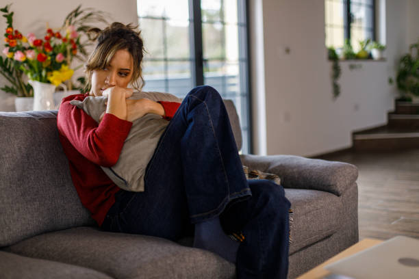 istock Young woman sitting on the sofa, embracing a pillow while feeling anxious 1477558393