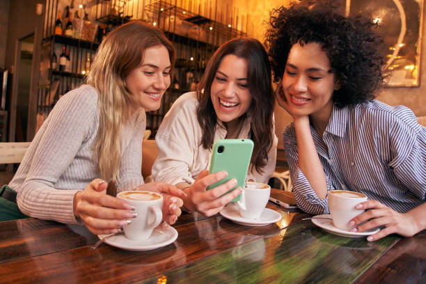 tres amigos que usan el teléfono celular se divierten tomando una copa en la cafetería. redes sociales de mujeres millennials. - mobile phone coffee shop group of people women fotografías e imágenes de stock