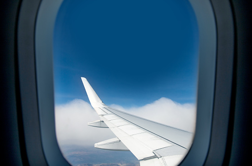 Sky view from inside the plane. Airplane window and airplane wing are visible in the foreground. The sky is visible in the background. Photo taken during the flight. Daytime hours.
