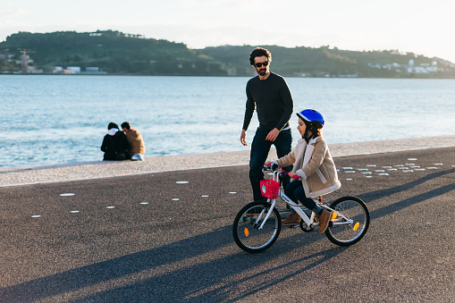 Lisbon, Portugal - January 2018 father on a skateboard with his son who rides a bicycle on the river bank