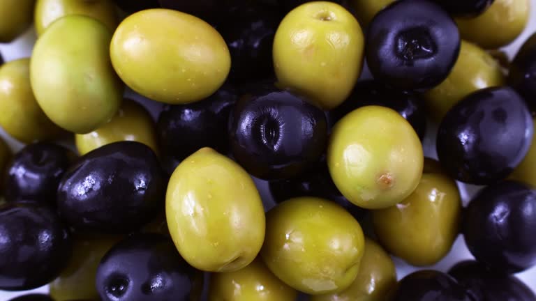 Top view of many green and black marinated whole olives circle rotation close up