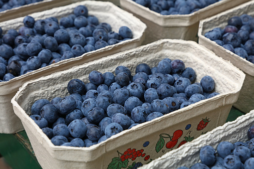 Close up fresh blueberry berries in paper container on retail display of farmers market, high angle view