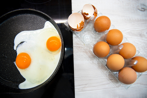 Eggs frying in black cooking pan and egg shells on kitchen counter. Above close up view on Breakfast preparation