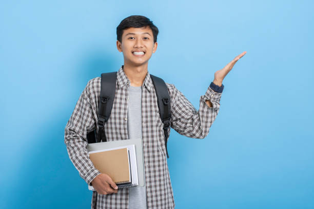 istock Young asian college student carrying backpack showing present product and advertising with hands isolated over blue background 1477580228