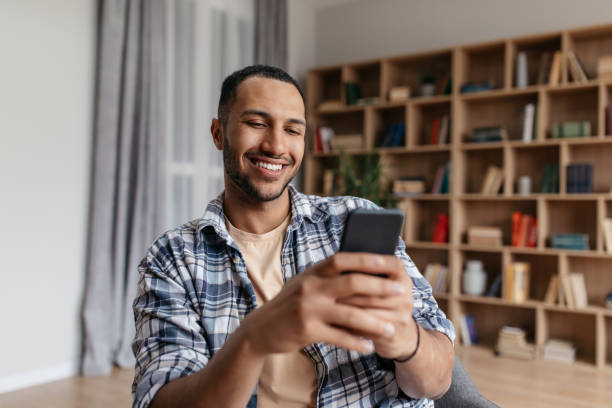 istock Enjoying free time. Happy arab man using smartphone while sitting on chair at home, relaxing in living room 1477580854